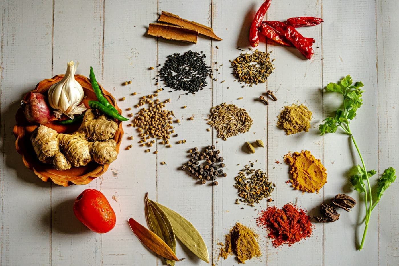 Whole spices, garlic, and ginger arranged on a pale wooden surface.